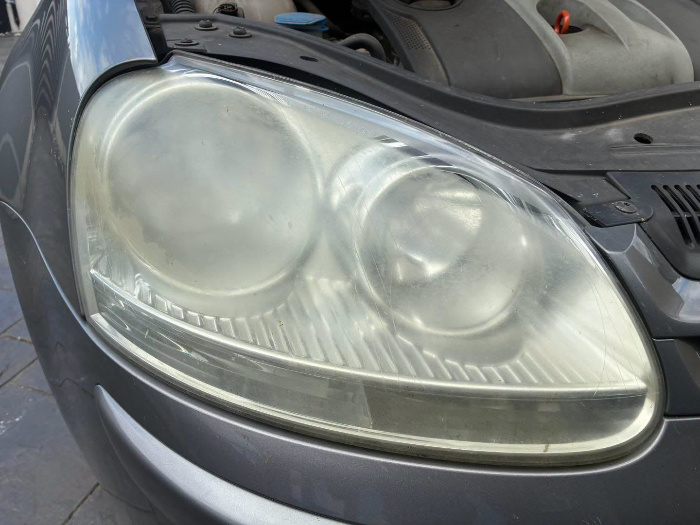 Before restoration: cloudy, yellowed headlight lens on a dark Volkswagen